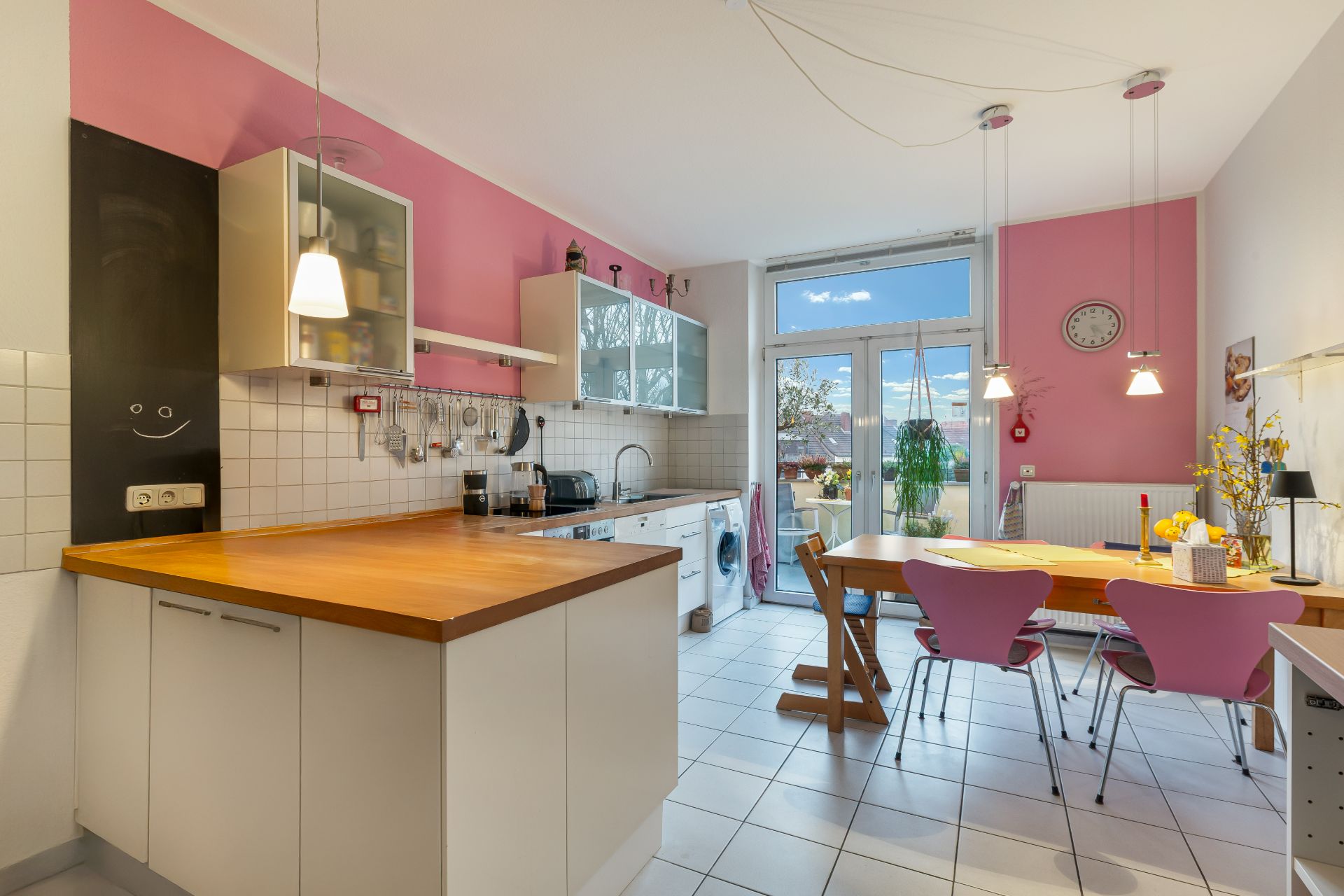Helle Küche mit rosa Wänden, Holztisch, Stühlen und Zugang zu einem Balkon.