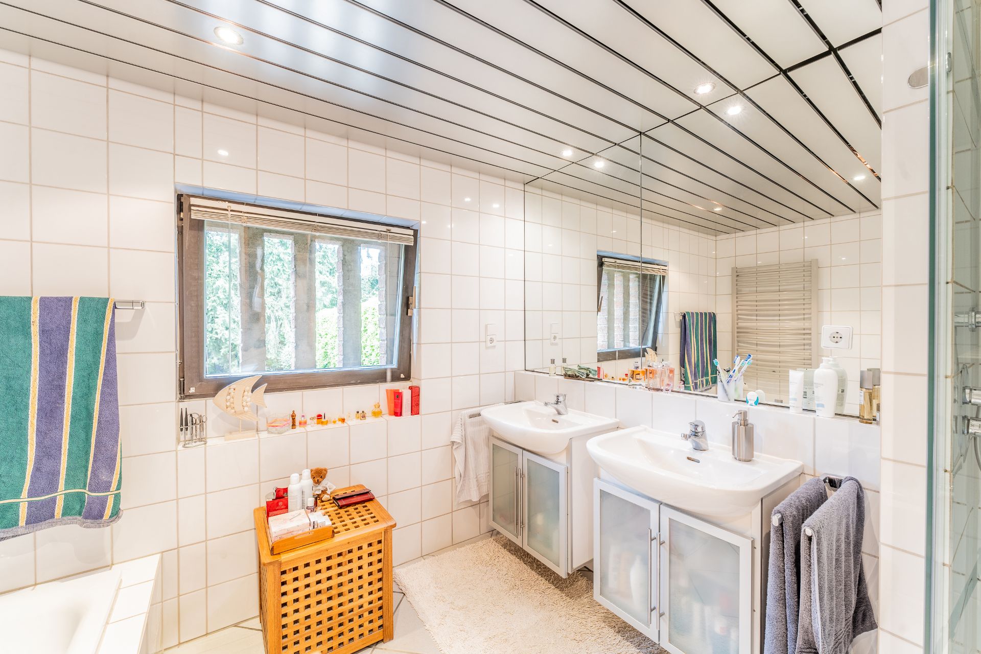 Helles Badezimmer mit zwei Waschbecken, großem Spiegel, Fenster und weißen Fliesen.