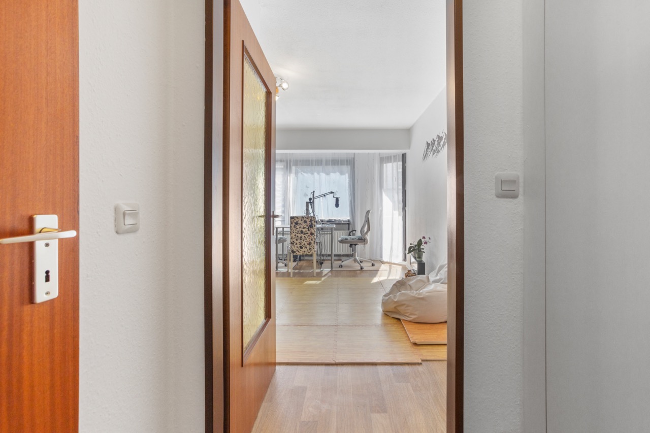 Blick durch geöffnete Tür in ein helles Zimmer mit Schreibtisch, Stuhl und Sitzsack.