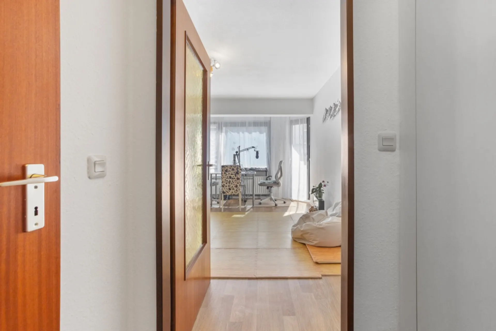 Blick durch geöffnete Tür in ein helles Zimmer mit Schreibtisch, Stuhl und Sitzsack.