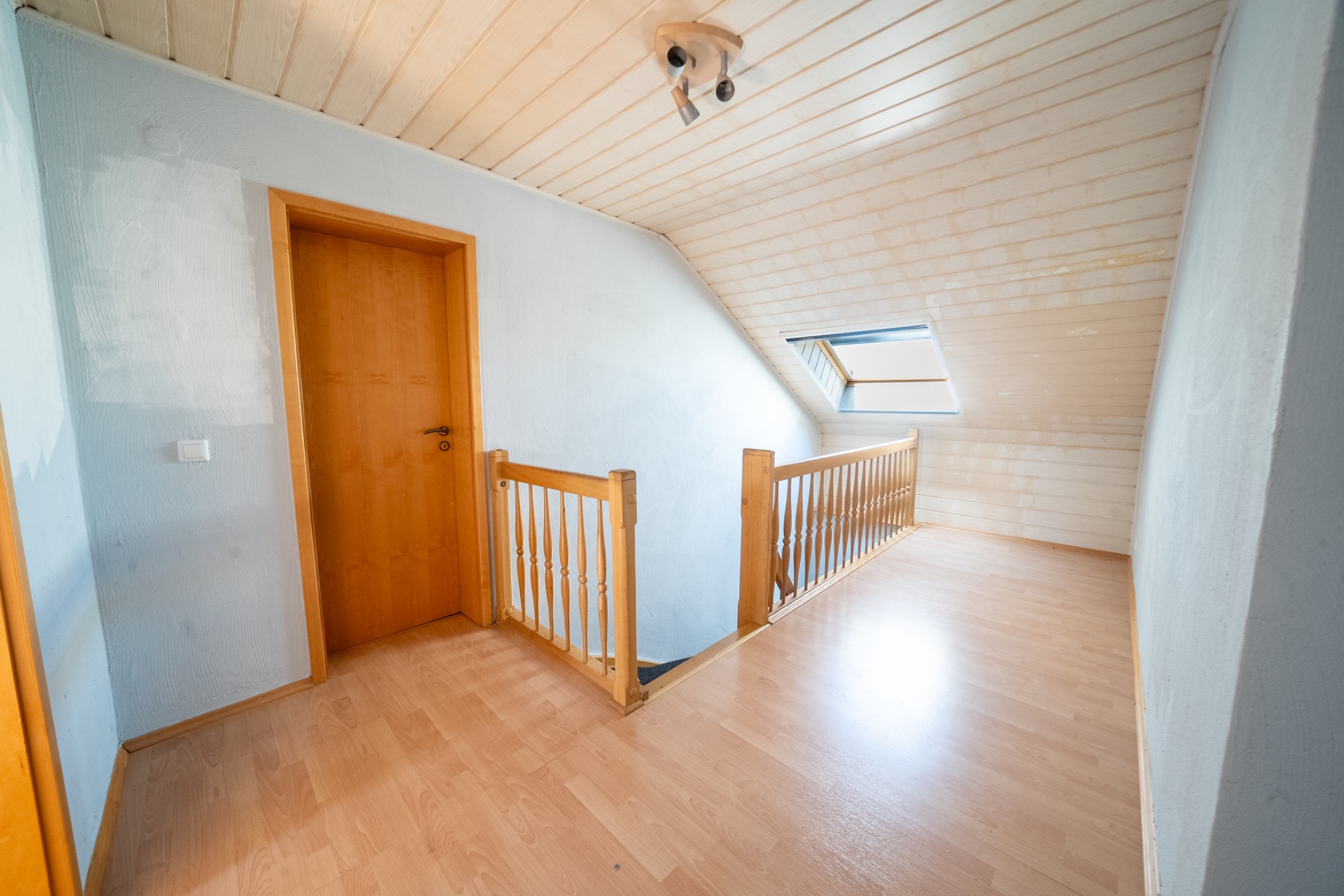 Heller Flur im Dachgeschoss mit Holzgeländer, Tür und Dachfenster.