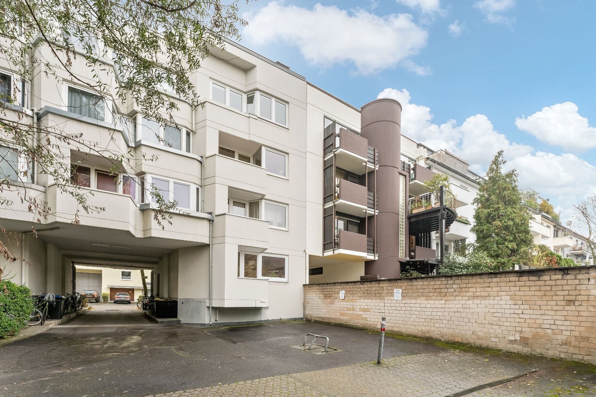 Mehrstöckiges Wohngebäude mit Balkonen, Einfahrt und geparkten Fahrrädern am Haus.
