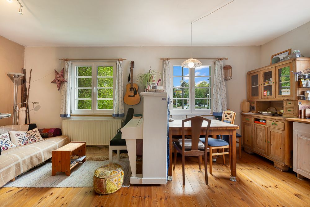 Wohnzimmer mit Sofa, Esstisch, Klavier, Gitarre und Holzschrank auf Holzboden.