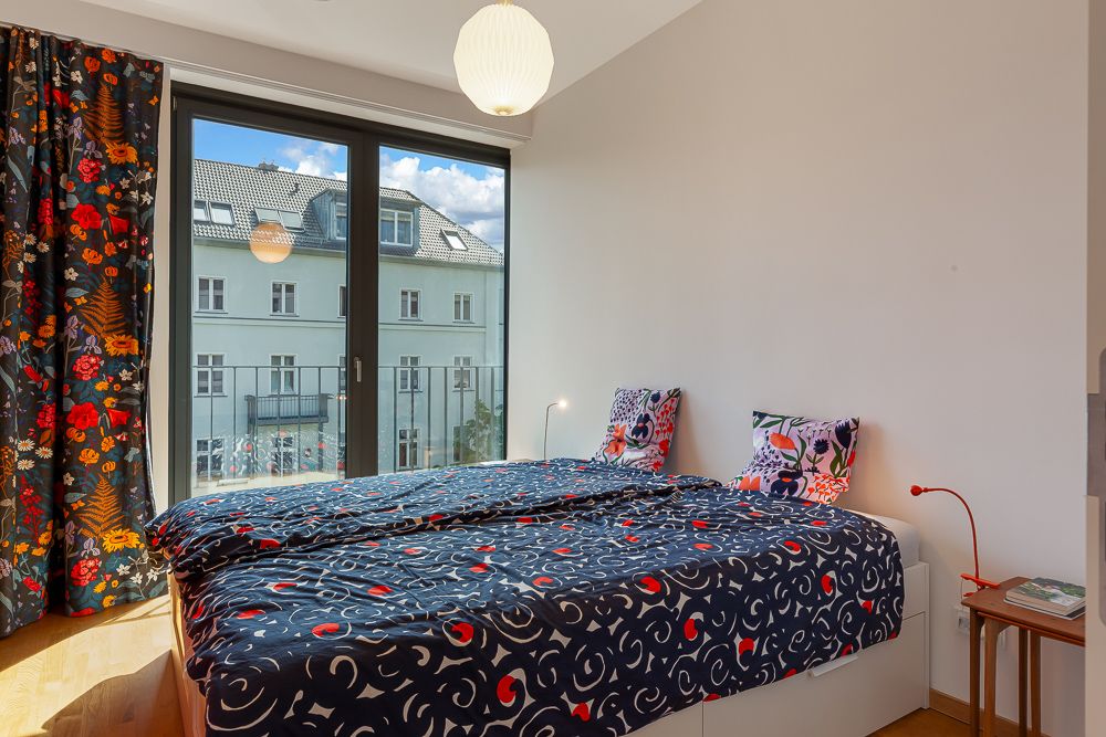 Schlafzimmer mit Doppelbett, bunte Bettwäsche, großer Fensterfront und bunter Vorhänge.
