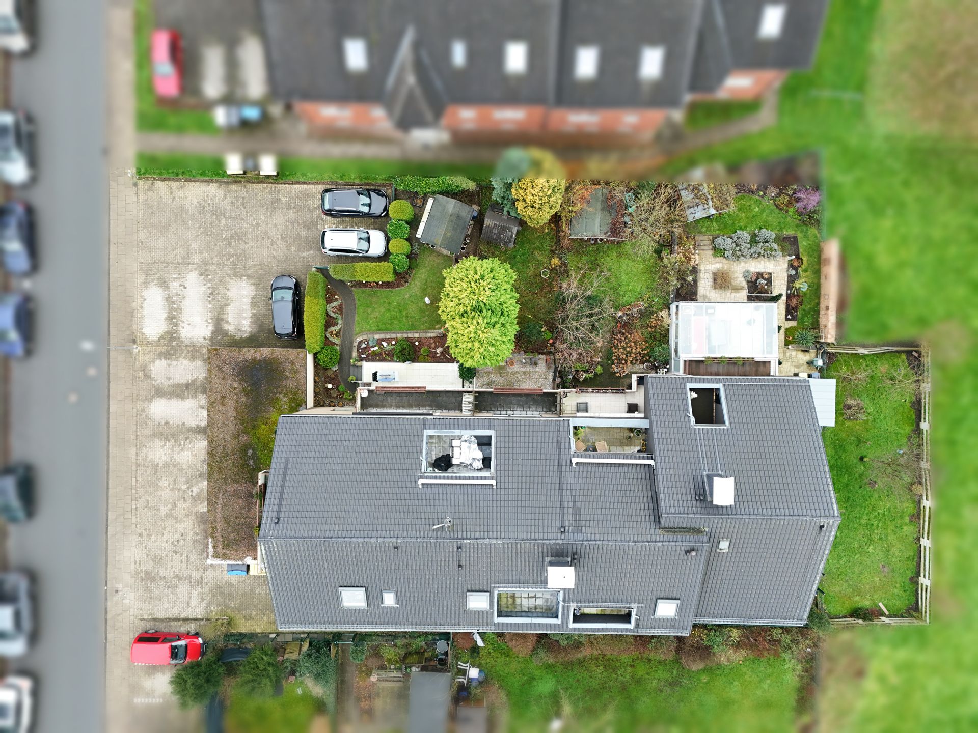 Luftaufnahme eines Wohnhauses mit Garten, Autoeinfahrt und mehreren geparkten Autos.