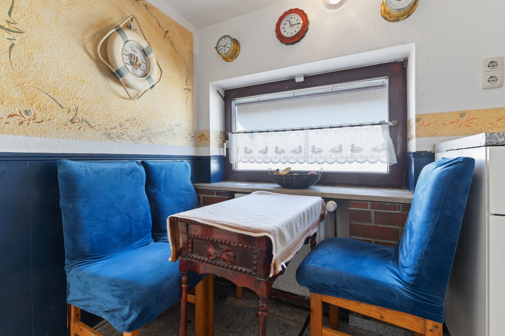 Kleiner Essbereich mit blau bezogenen Stühlen, Tisch am Fenster und maritimer Wanddekoration.