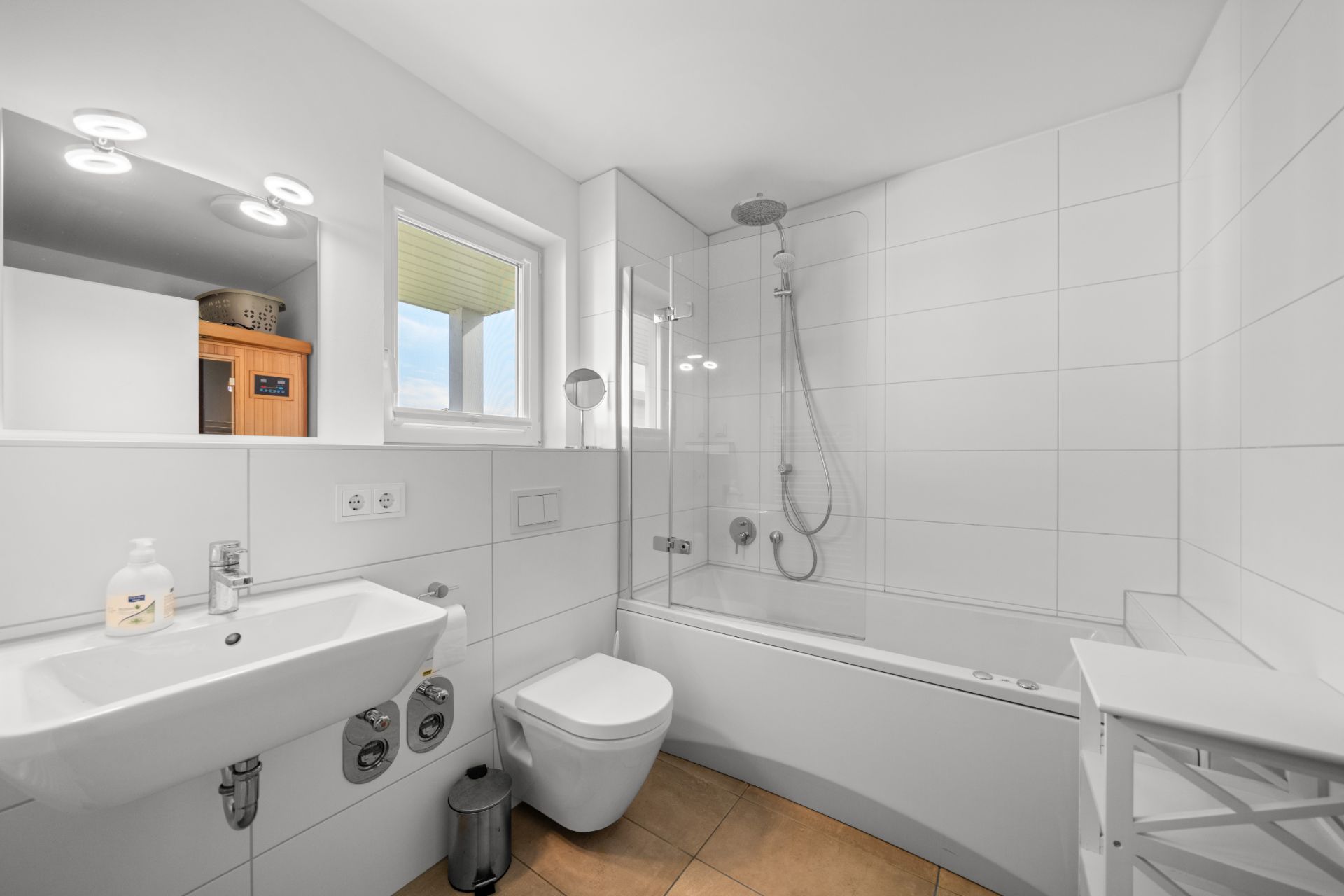 Modernes Bad mit weißer Badewanne, Dusche, Waschbecken, WC und Fenster.