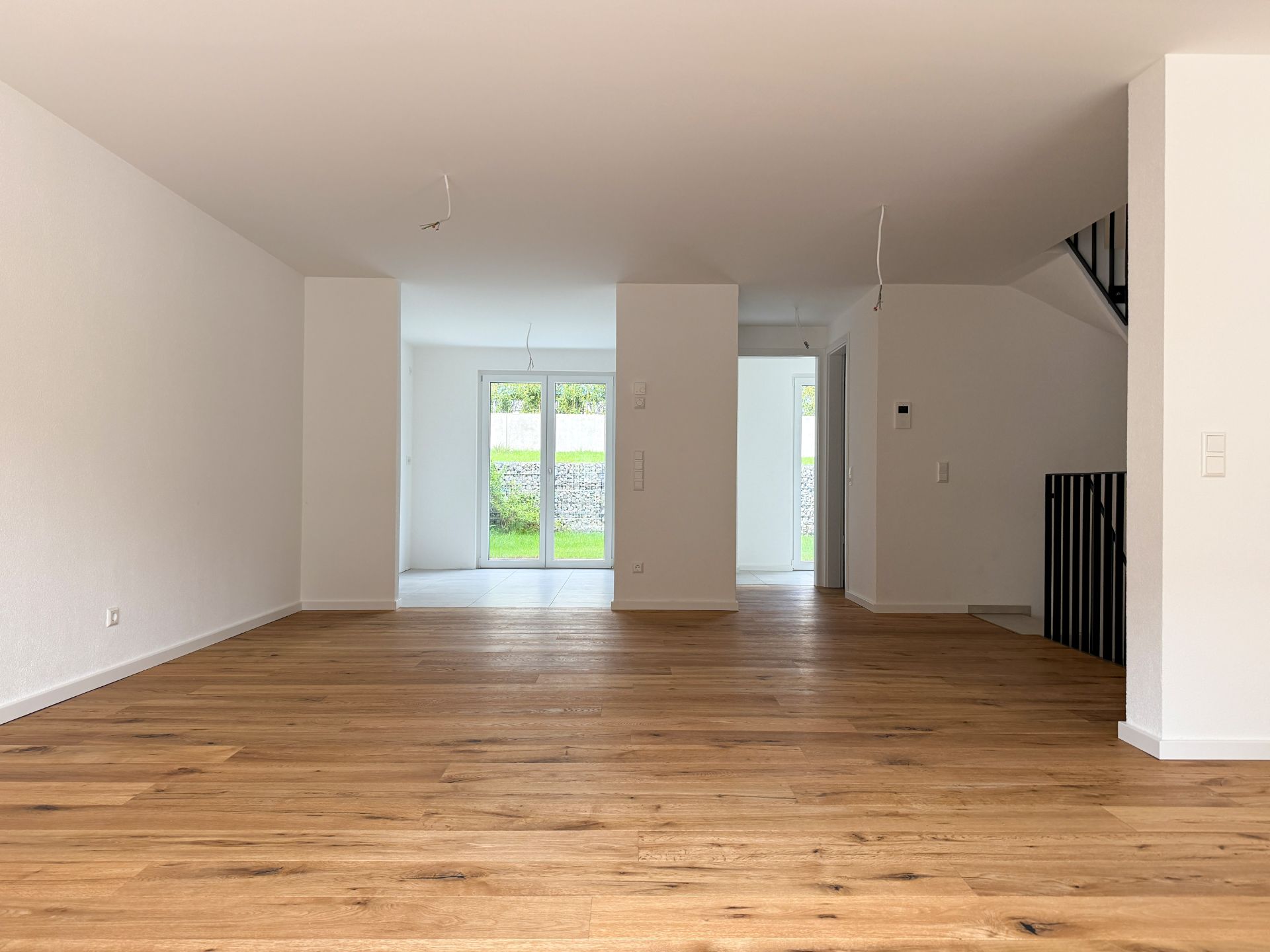 Helles Wohnzimmer mit Holzfußboden, großen Fenstern und Treppe nach oben.