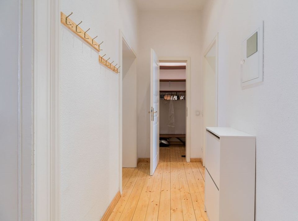 Heller Flur mit Holzboden, Garderobenhaken und weißem Schrank.