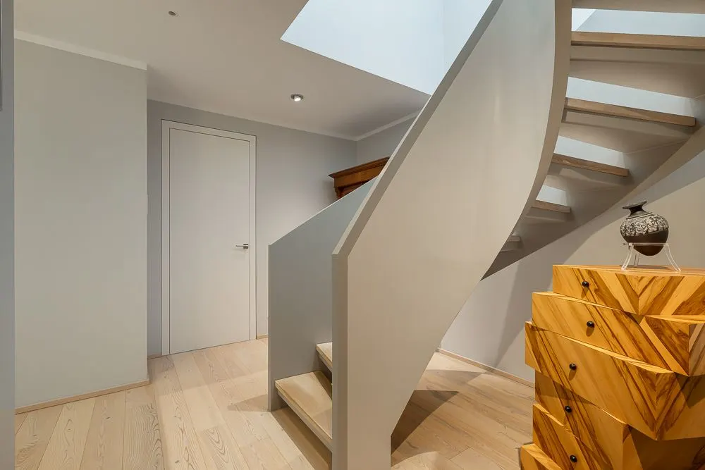 Helle Diele mit Holztreppe, weißer Tür und einer gemusterten Kommode.