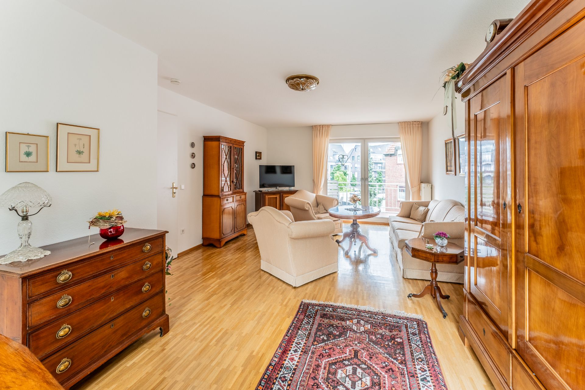 Helles Wohnzimmer mit Holzmöbeln, Teppich, Sofas und Zugang zu einem Balkon.