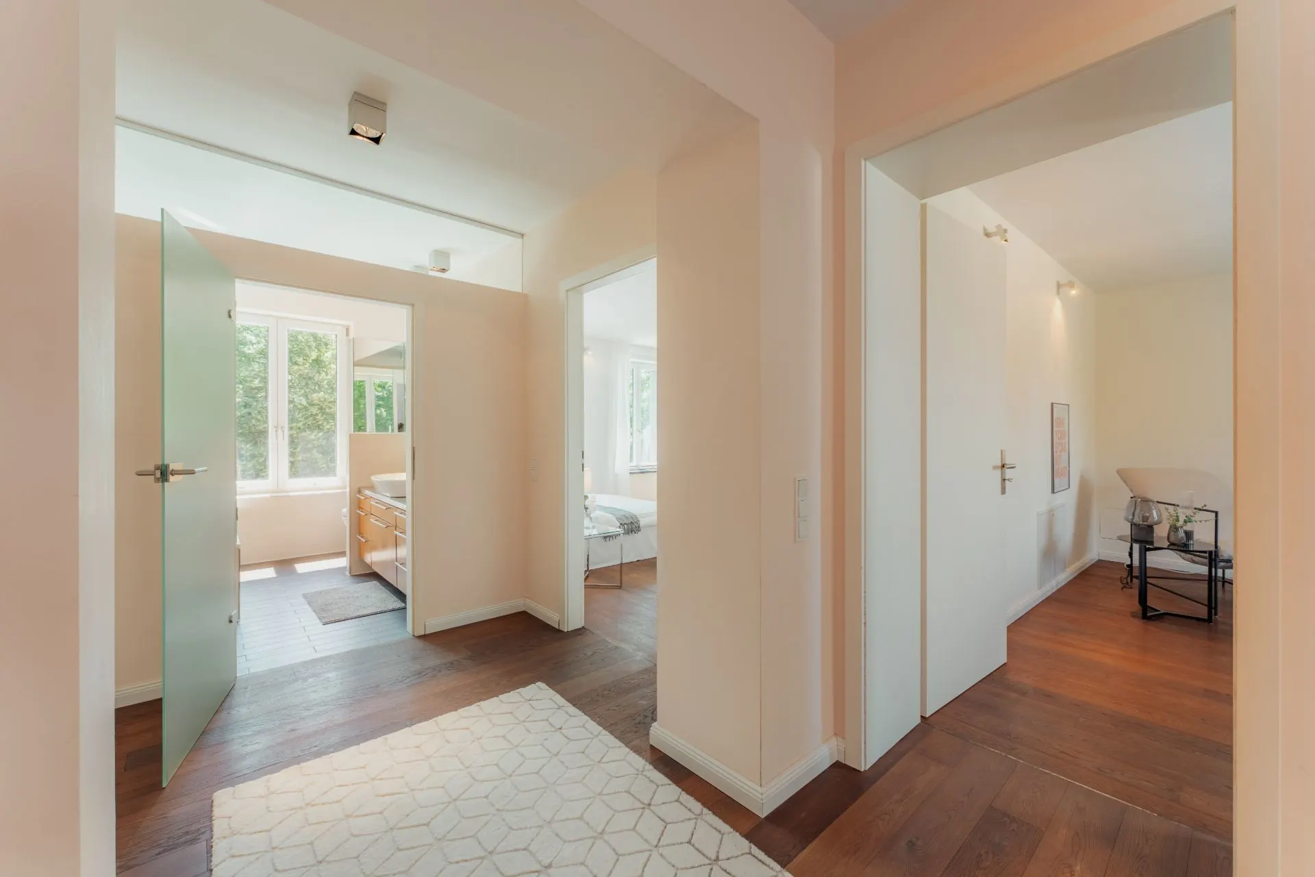 Heller Flur mit Holzboden, zwei offenen Türen zu Zimmern und großem Fenster im Hintergrund.