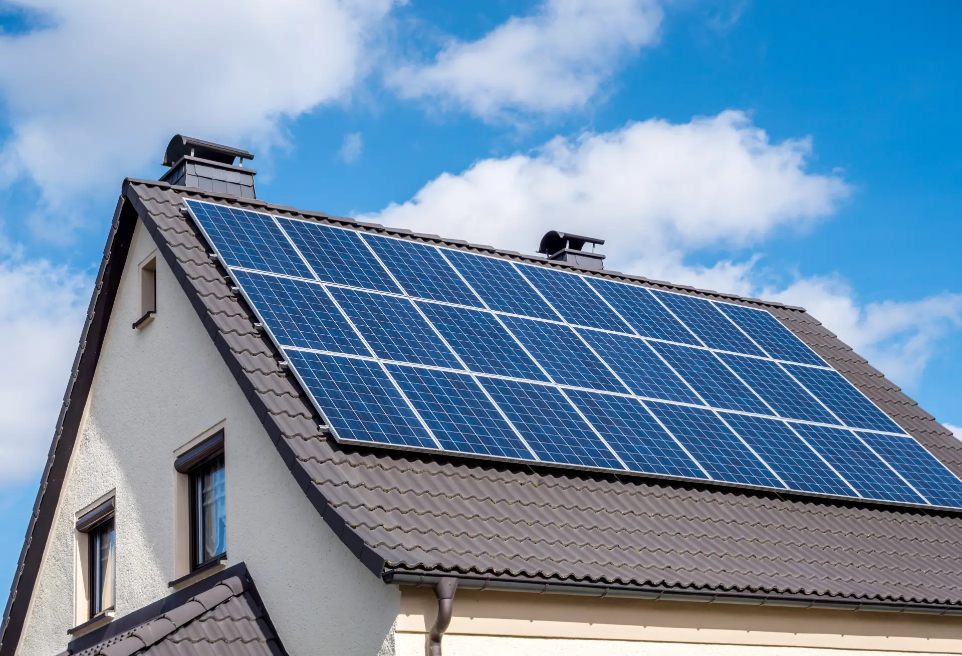 Dach eines Wohnhauses mit vielen Solarpanels unter blauem Himmel.