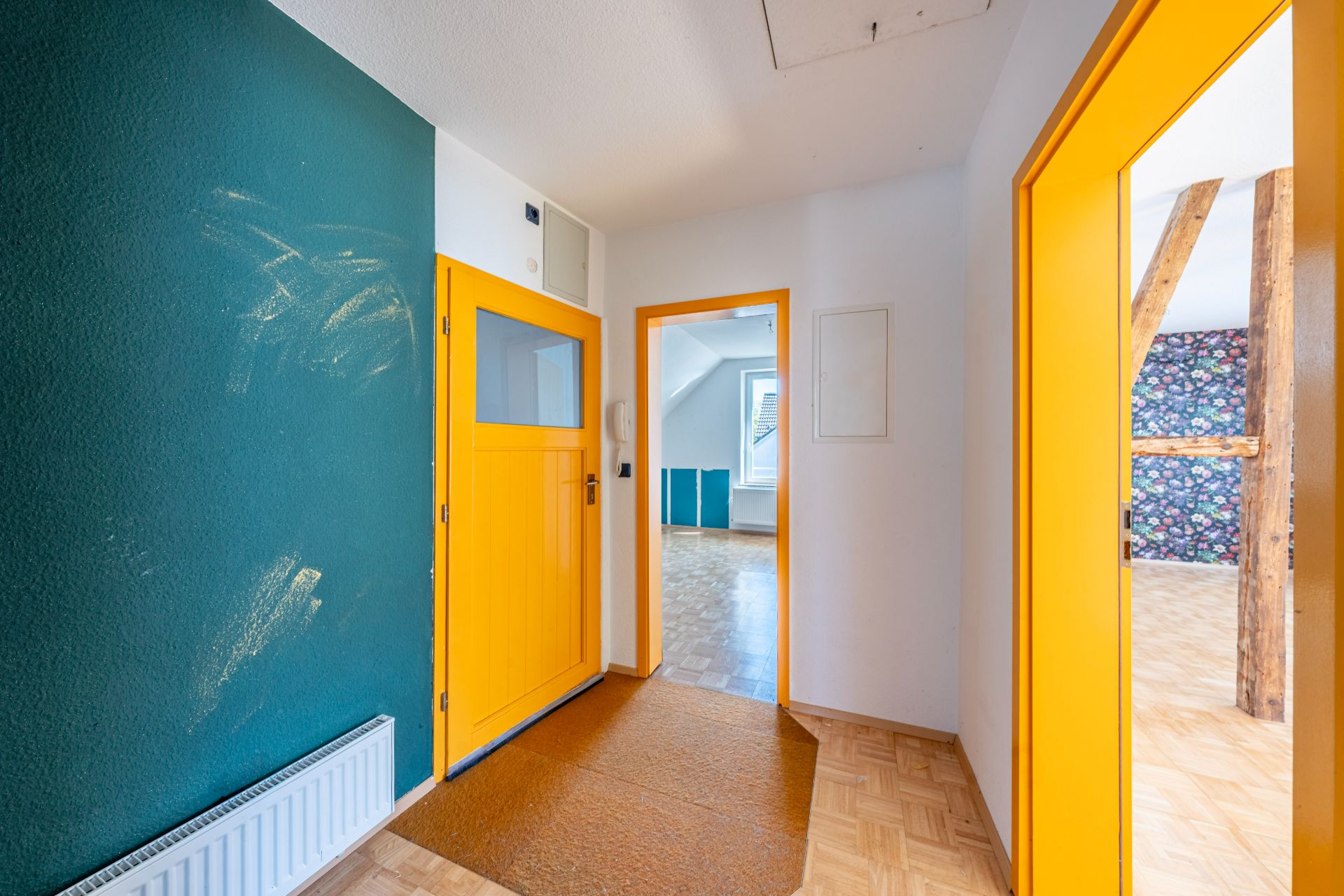 Flur mit gelber Tür, grüner Wand und Blick in helle Zimmer mit Holzboden und sichtbaren Balken.