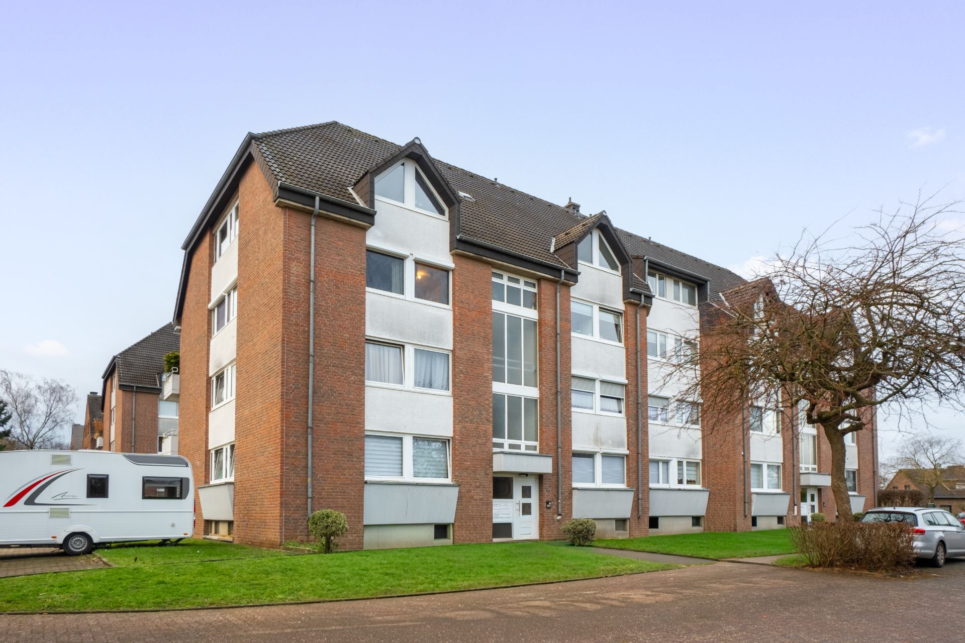 Mehrfamilienhaus mit roter Fassade, mehreren Fenstern und gepflegtem Vorgarten.