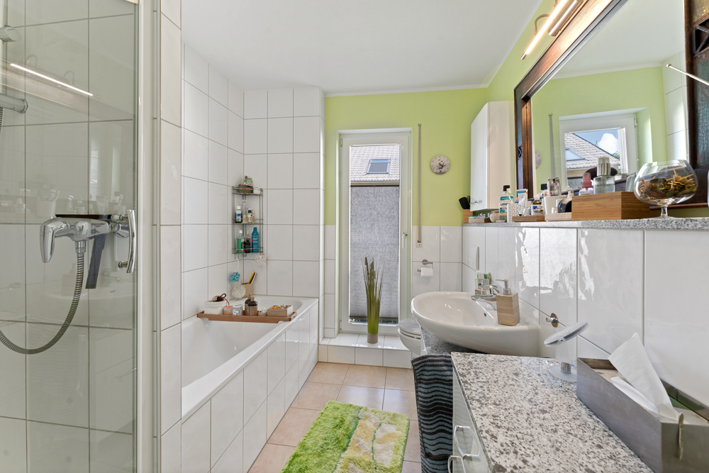 Modernes Badezimmer mit Badewanne, Dusche, Waschbecken und großem Spiegel.