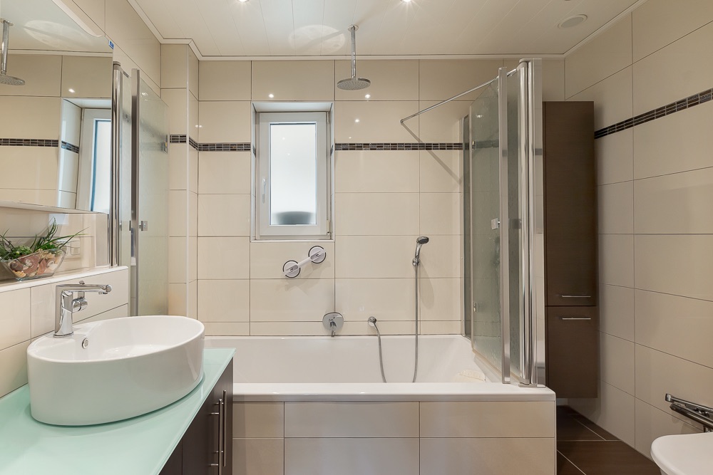 Modernes Badezimmer mit Badewanne, Glasduschwand, Waschbecken und kleinem Fenster.
