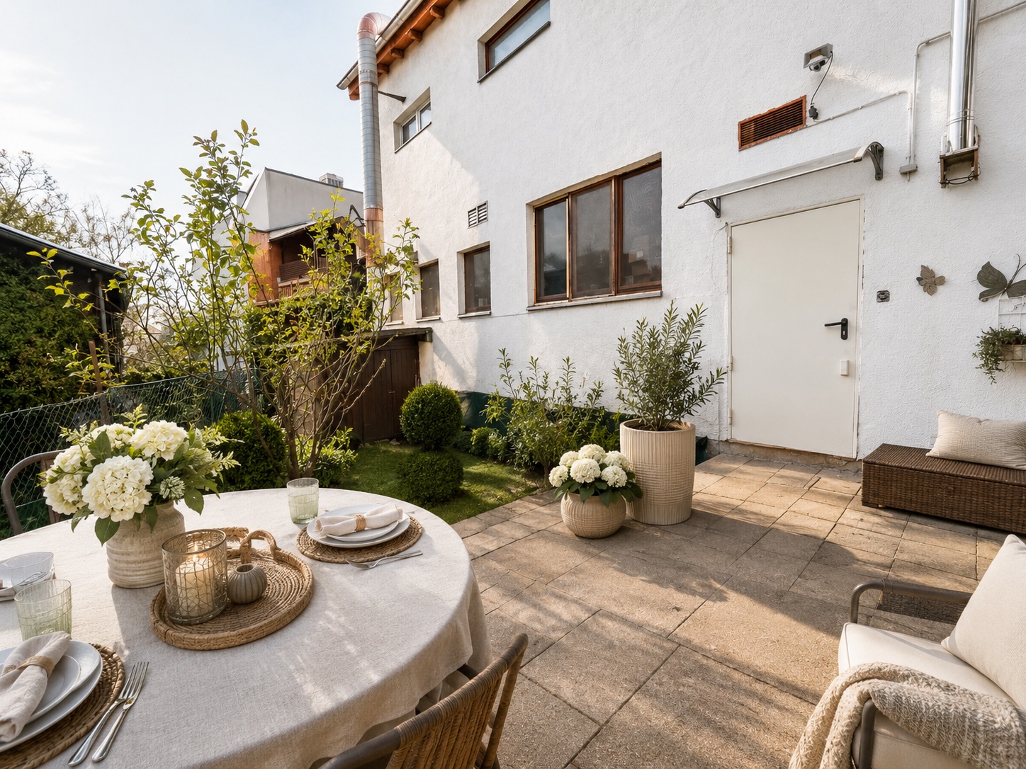 Gepflegte Terrasse mit Esstisch, Blumen und Sitzbank vor einem weißen Wohnhaus.