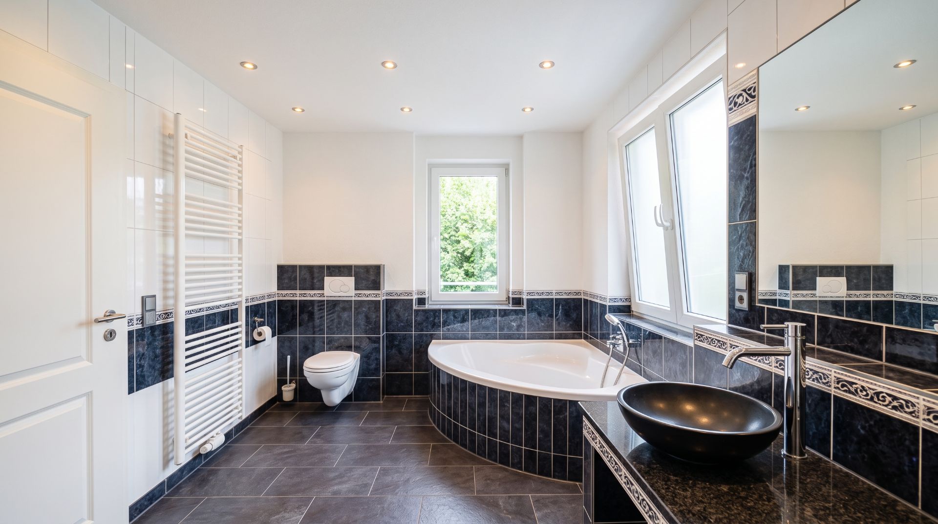 Modernes Badezimmer mit Eckbadewanne, Waschbecken, WC, Fenster und großem Spiegel.