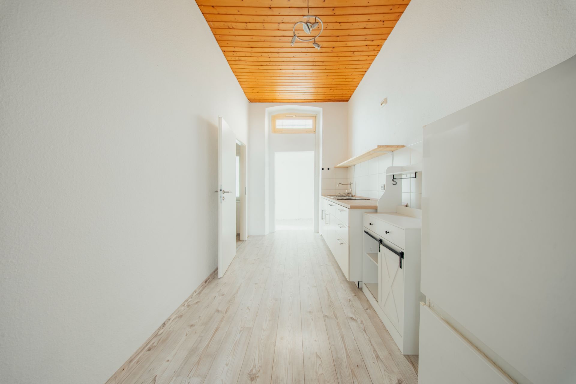 Helle, schmale Küche mit Holzdecke, weißen Wänden und modernen Einbaugeräten.
