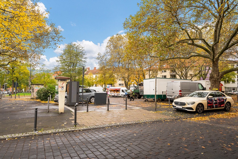 Parkplatz mit Autos und Bäumen im Herbst, im Hintergrund Wohngebäude.