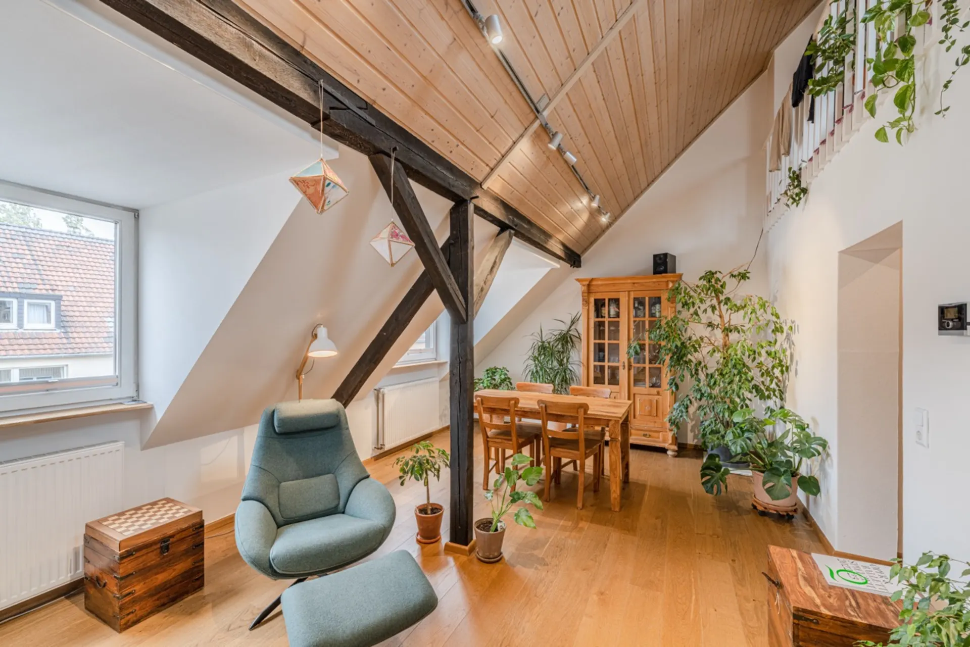 Heller Dachgeschossraum mit Sessel, Esstisch, Holzschrank und vielen Pflanzen.