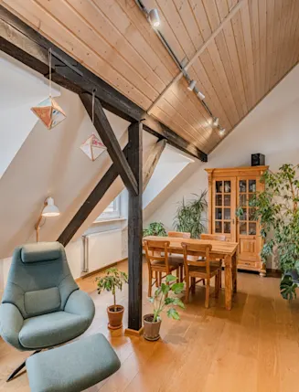 Heller Dachgeschossraum mit Sessel, Esstisch, Holzschrank und vielen Pflanzen.