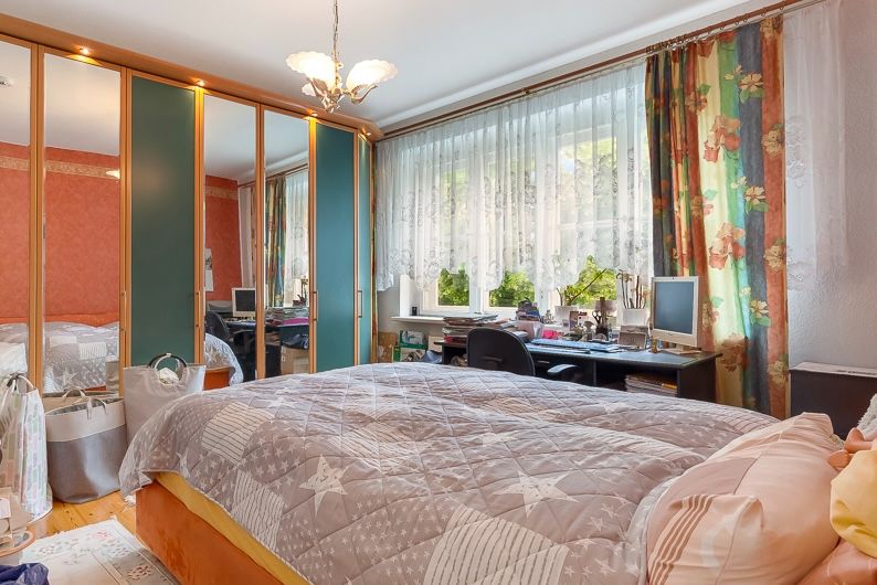 Schlafzimmer mit großem Bett, Schreibtisch am Fenster und Spiegelschrank.