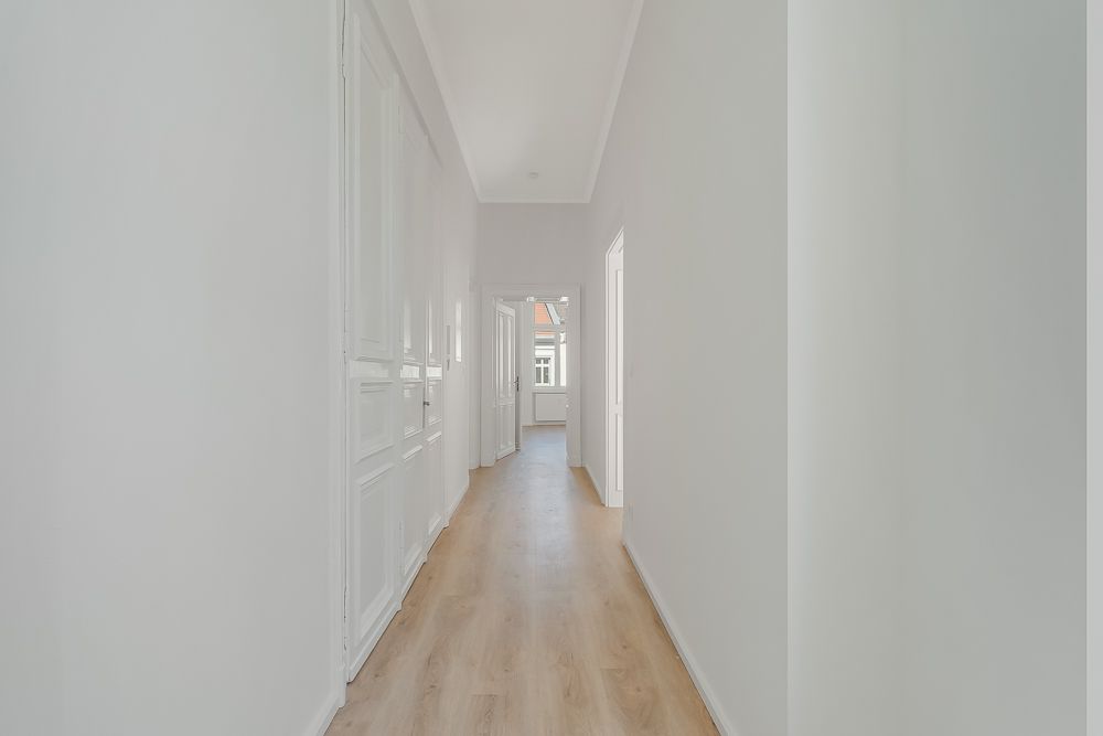 Langer, heller Flur mit Holzboden und weißen Türen in einer Wohnung.