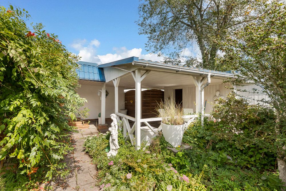 Überdachte Terrasse mit weißem Geländer, umgeben von grünem Garten und Pflanzen.