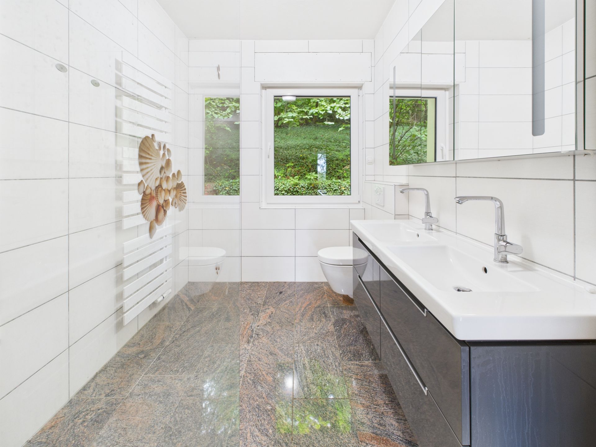 Modernes Badezimmer mit zwei Waschbecken, WC, Fenster und hellen Fliesen.