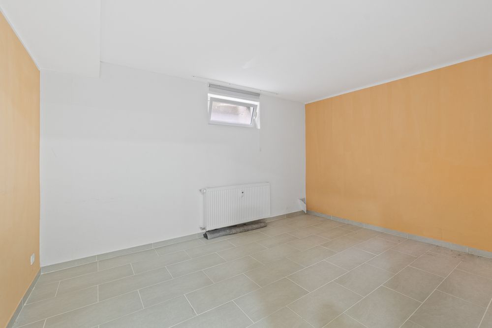 Leerer Raum mit beigen Fliesen, zwei orangefarbenen Wänden und kleinem Fenster.
