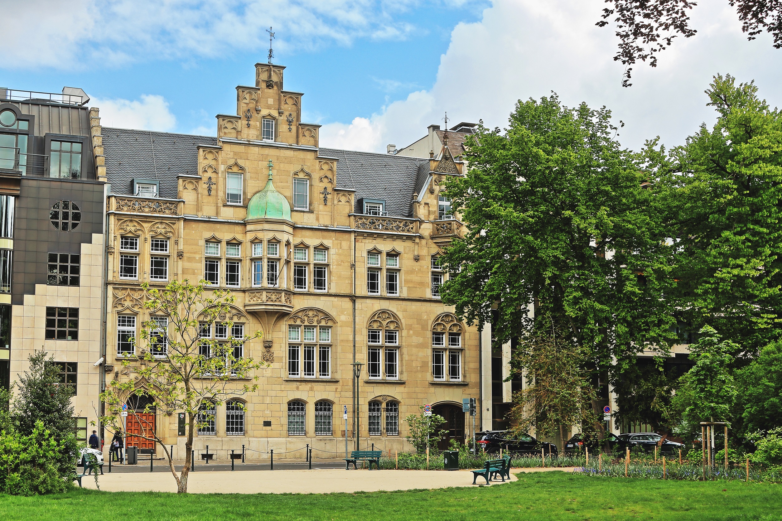 Historisches Wohngebäude mit aufwendigen Fassadendetails und kleinem Park im Vordergrund.