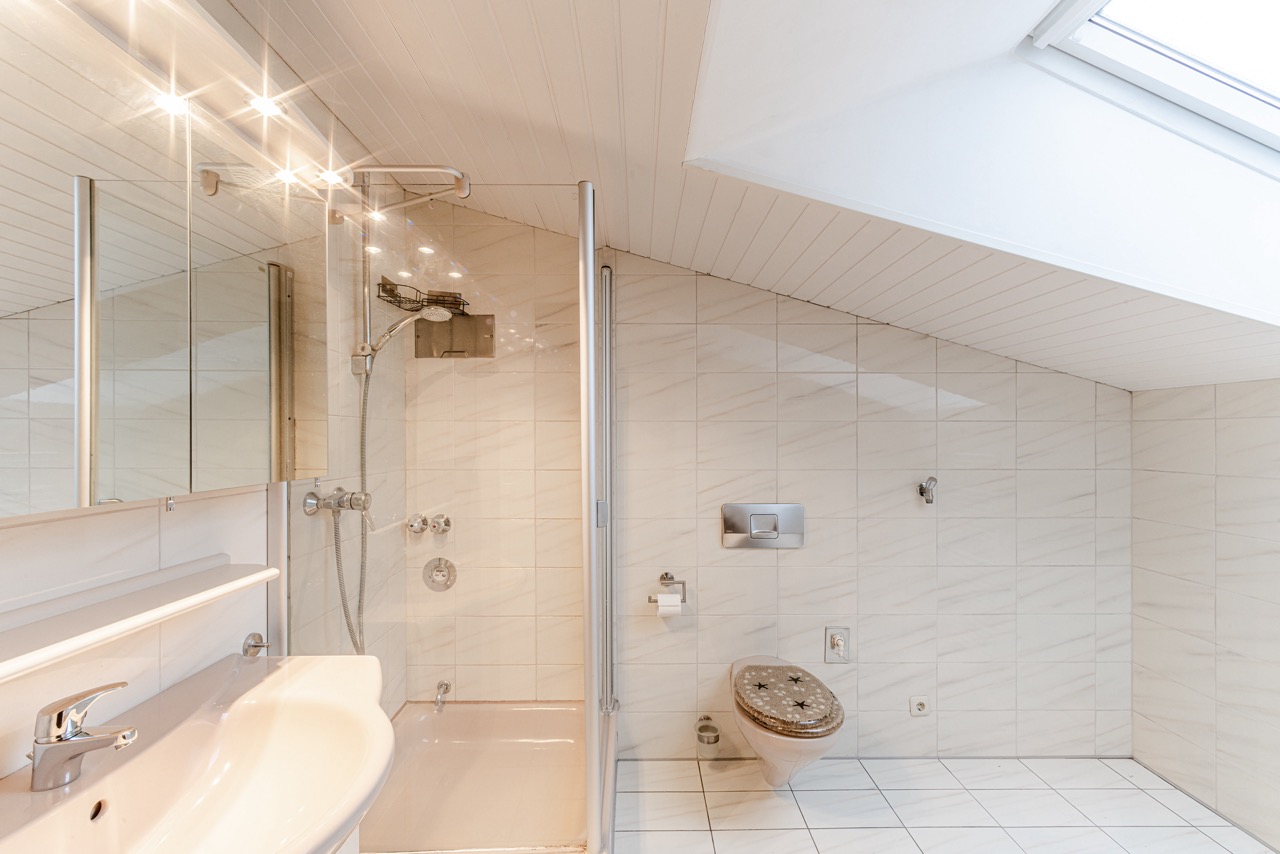 Modernes Badezimmer mit Dusche, Waschbecken, WC und Dachfenster unter einer Schräge.