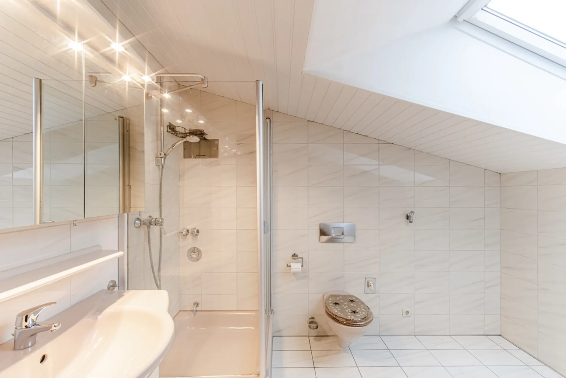 Modernes Badezimmer mit Dusche, Waschbecken, WC und Dachfenster unter einer Schräge.