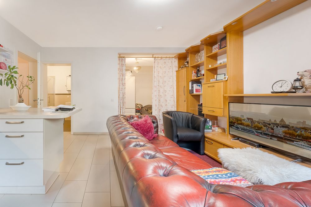Wohnzimmer mit rotem Ledersofa, Wandregal, Fernseher und offener Küche.