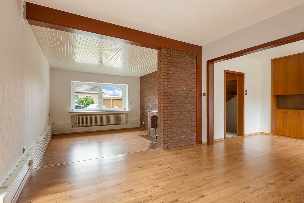 Helles Wohnzimmer mit Holzfußboden, großem Fenster und einer Trennwand aus rotem Backstein.