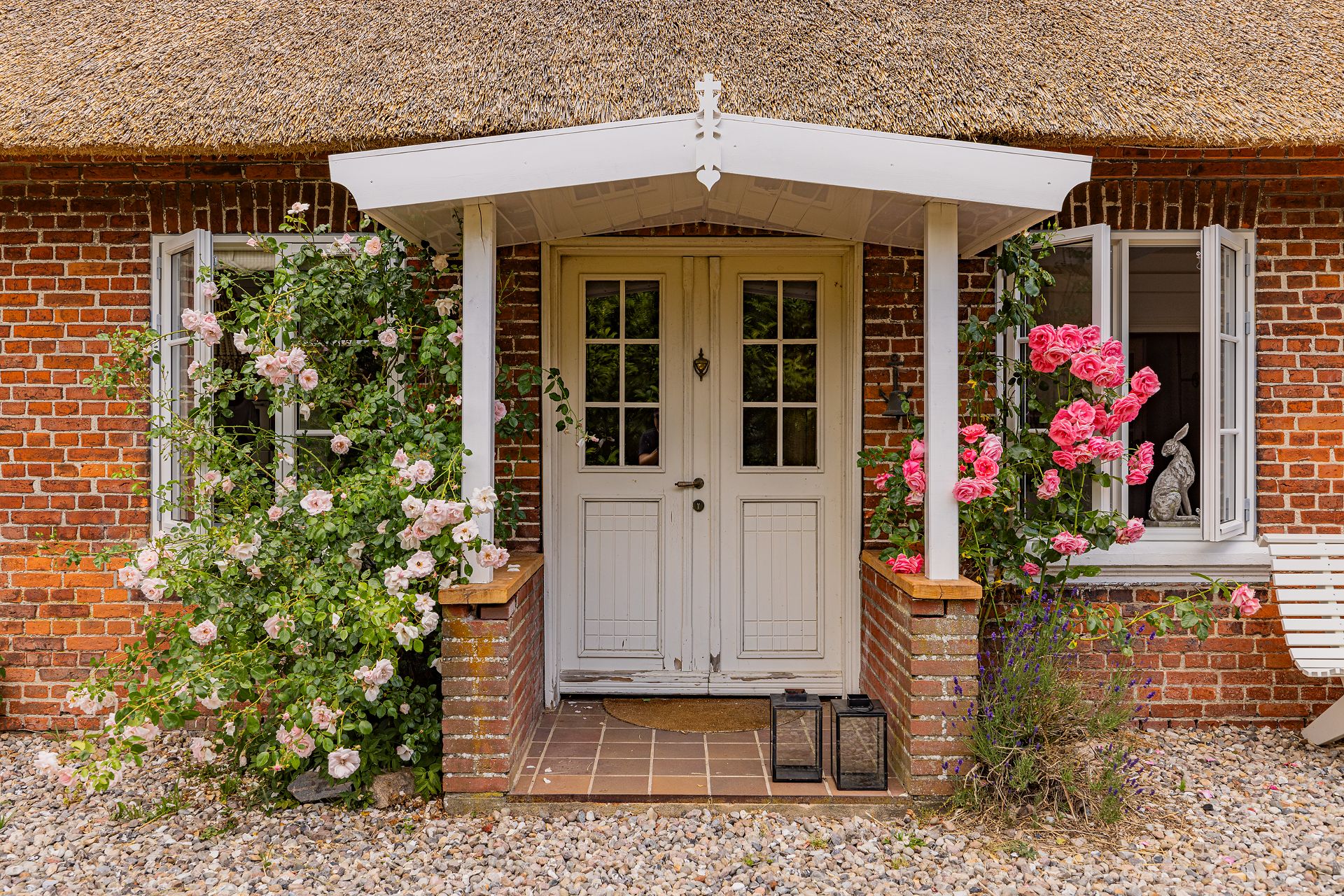 Eingangstür eines Backsteinhauses mit Blumenranken und offenen Fenstern.