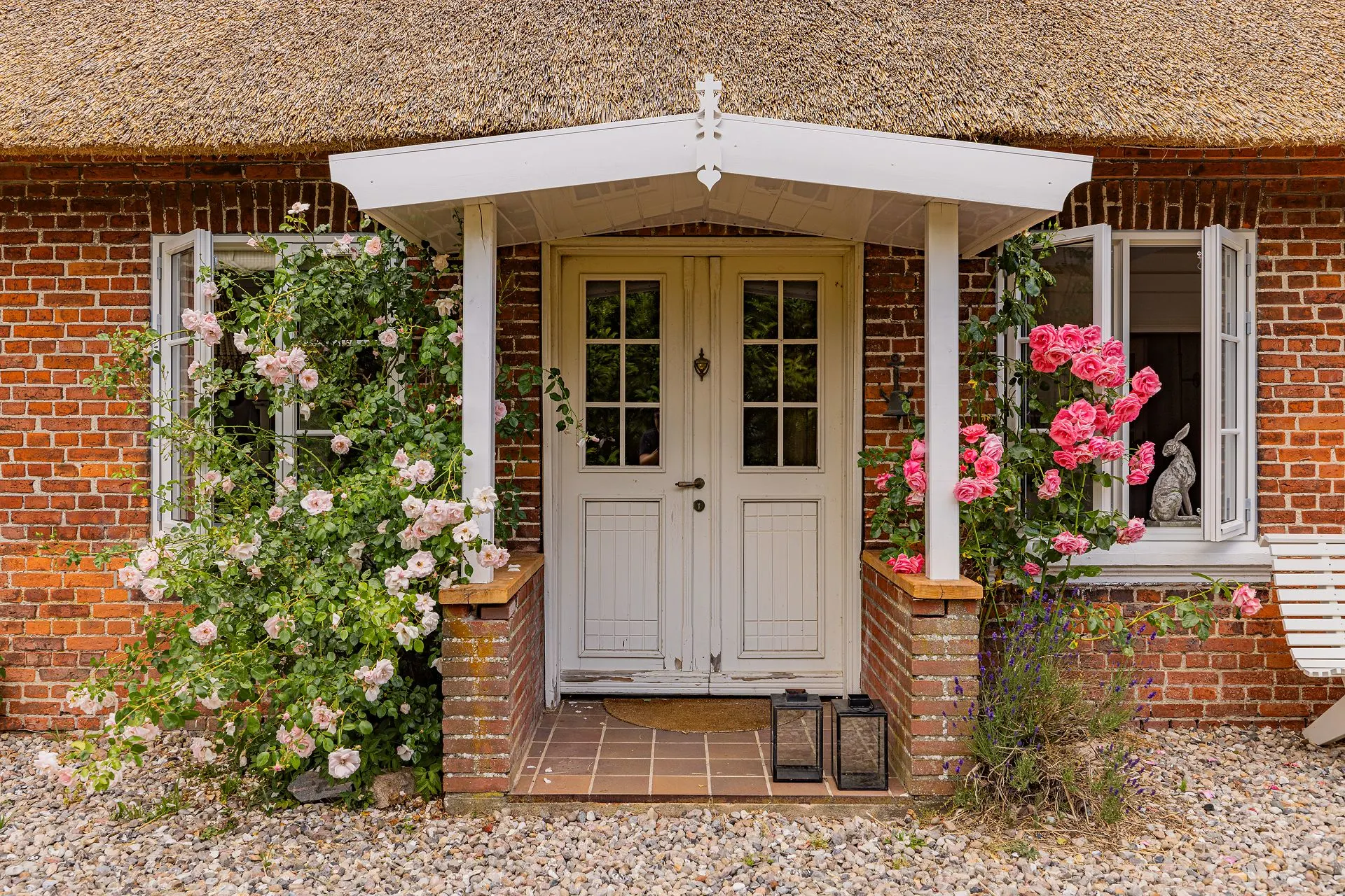 Eingangstür eines Backsteinhauses mit Blumenranken und offenen Fenstern.
