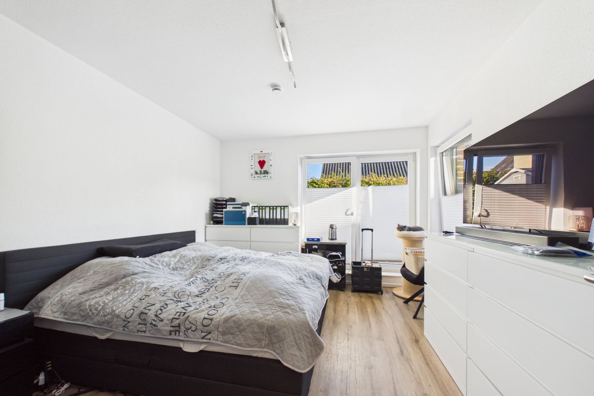Modernes Schlafzimmer mit Doppelbett, weißen Möbeln und großem Fenster mit Blick nach draußen.