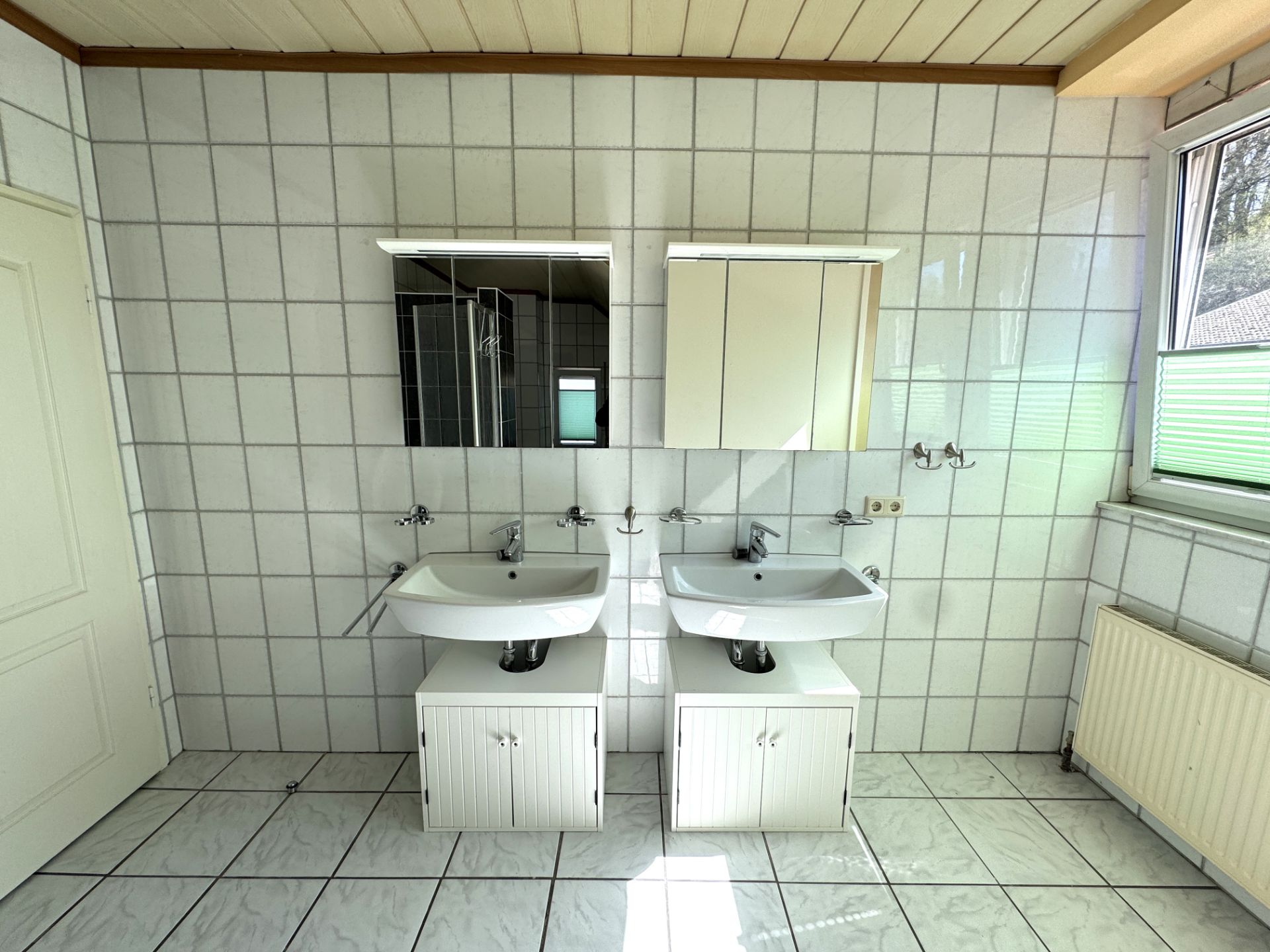 Zwei Waschbecken mit Unterschränken, Spiegeln und Fliesenwand in einem hellen Badezimmer.