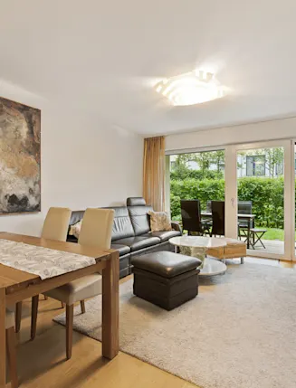 Modernes Wohnzimmer mit Esstisch, Sofa, TV, großem Gemälde und Zugang zur Terrasse mit Gartenblick.