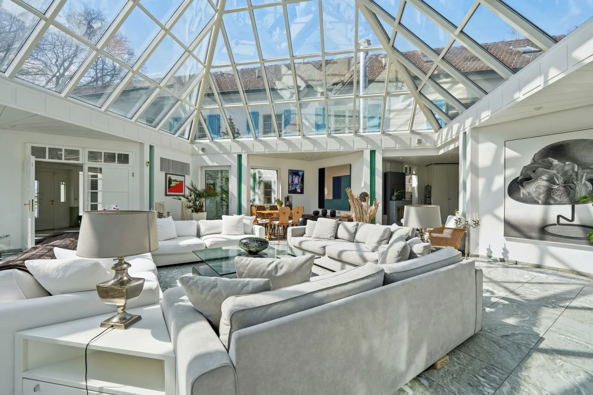 Heller Wohnraum mit Glasdach, weißen Sofas, Esstisch und moderner Kunst an der Wand.