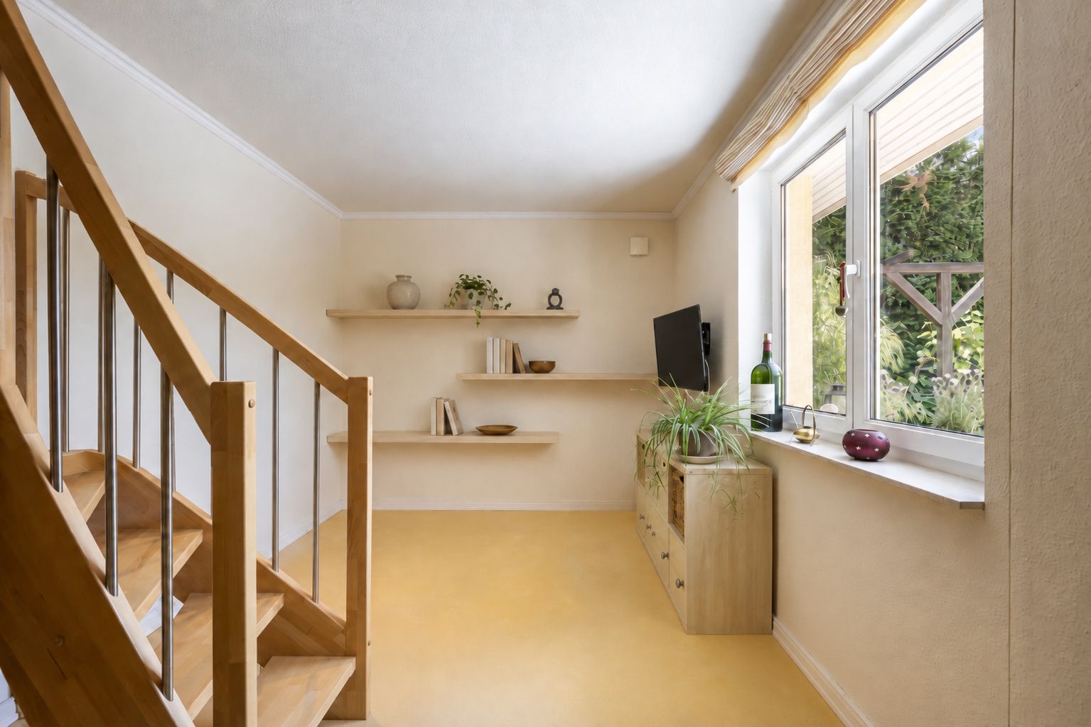 Heller Raum mit Holztreppe, Regal, Kommode, großem Fenster und Pflanzen.