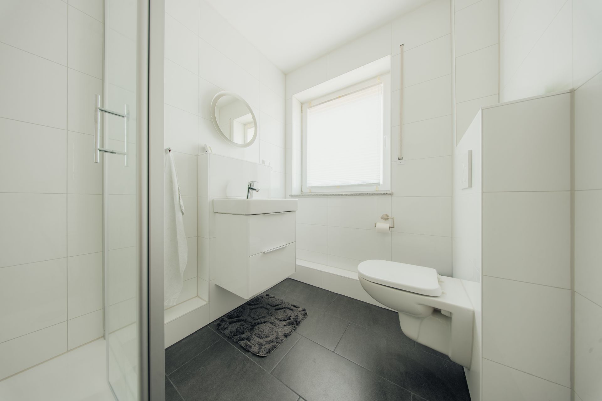 Modernes, weißes Badezimmer mit Dusche, Waschbecken, Wandspiegel und WC.