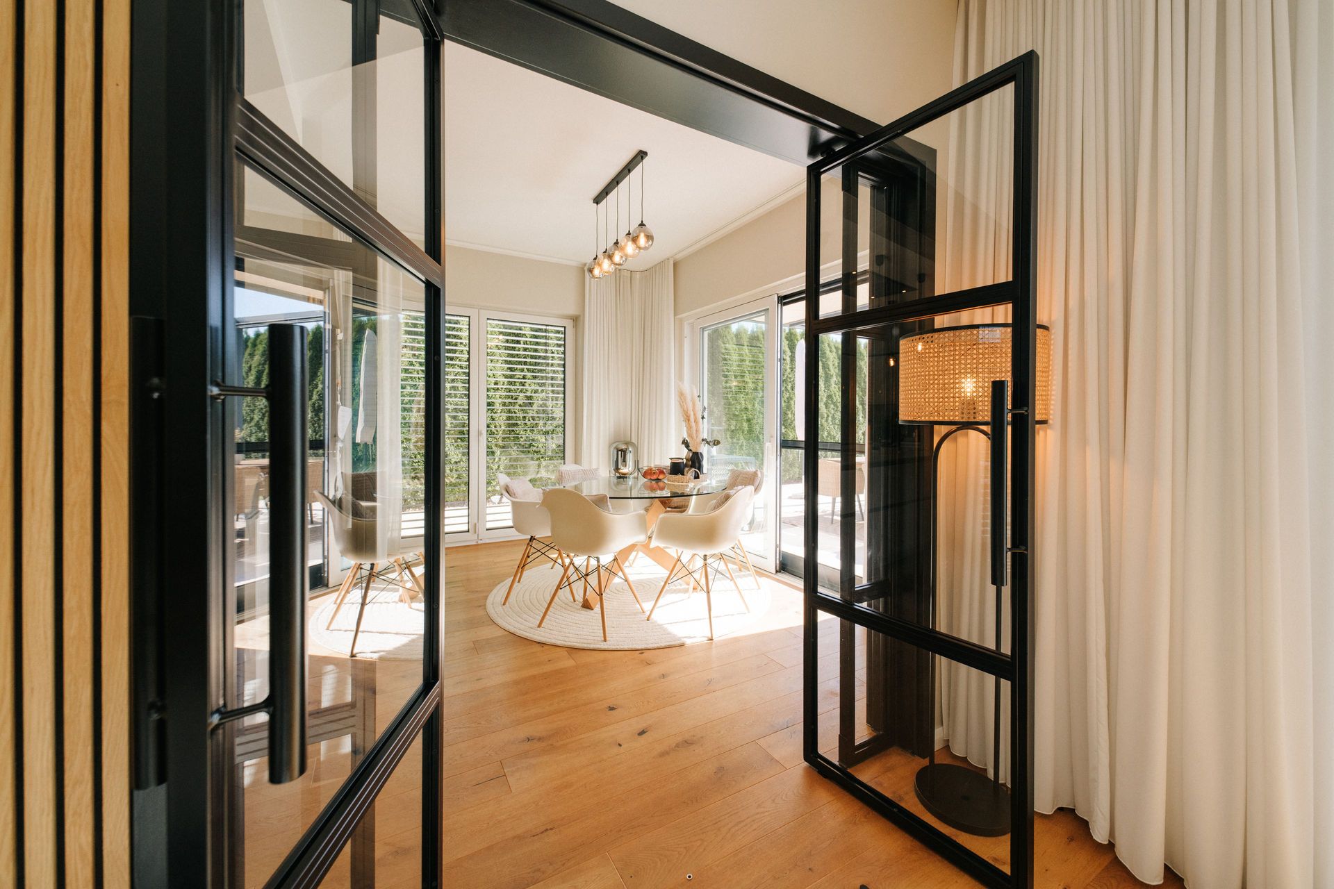 Heller Essbereich mit runden Tisch und weißen Stühlen auf Holzfußboden, große Fenster mit Vorhängen.