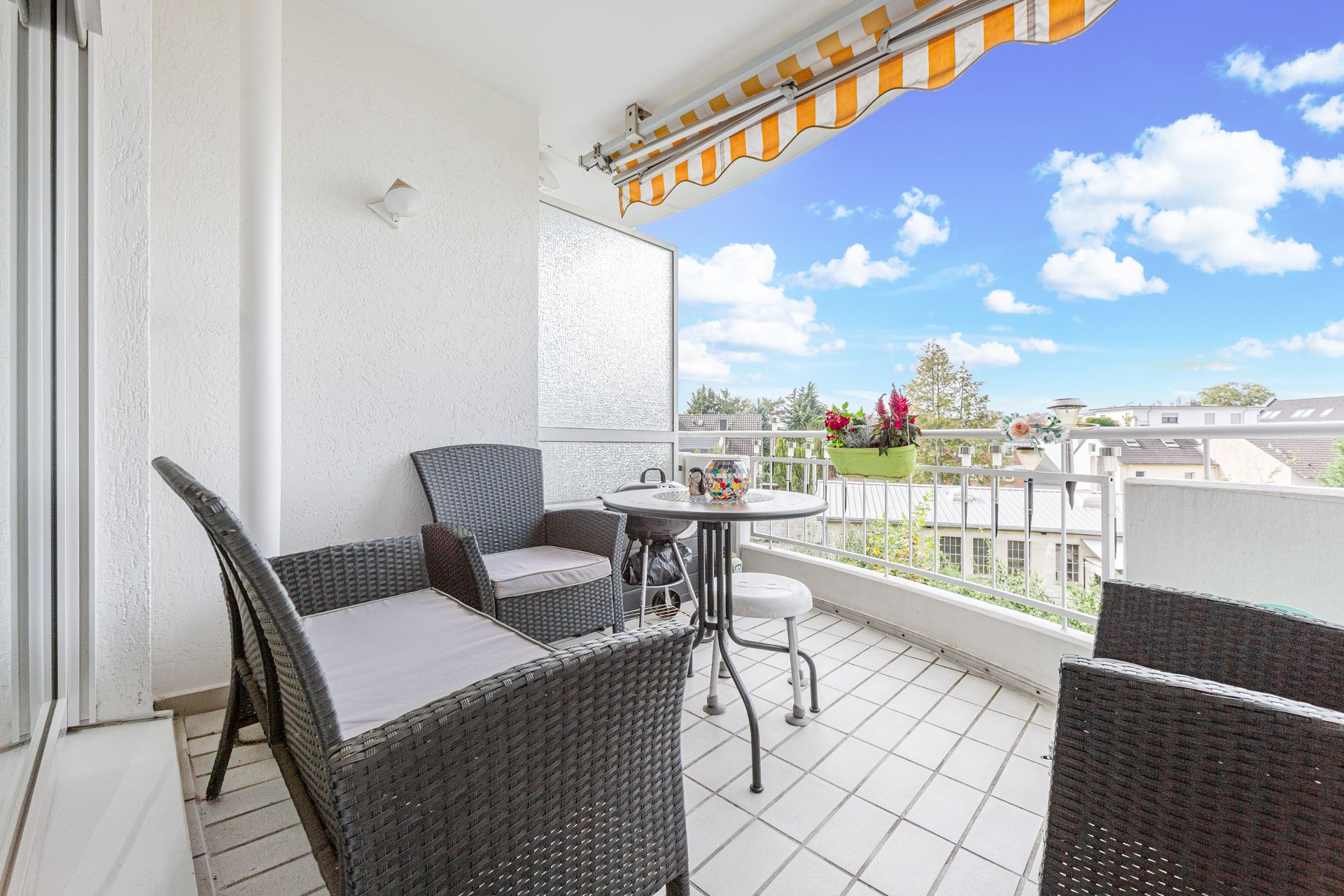 Heller Balkon mit Sitzgruppe, Tisch, Markise und Blumenkästen an einem Wohnhaus.