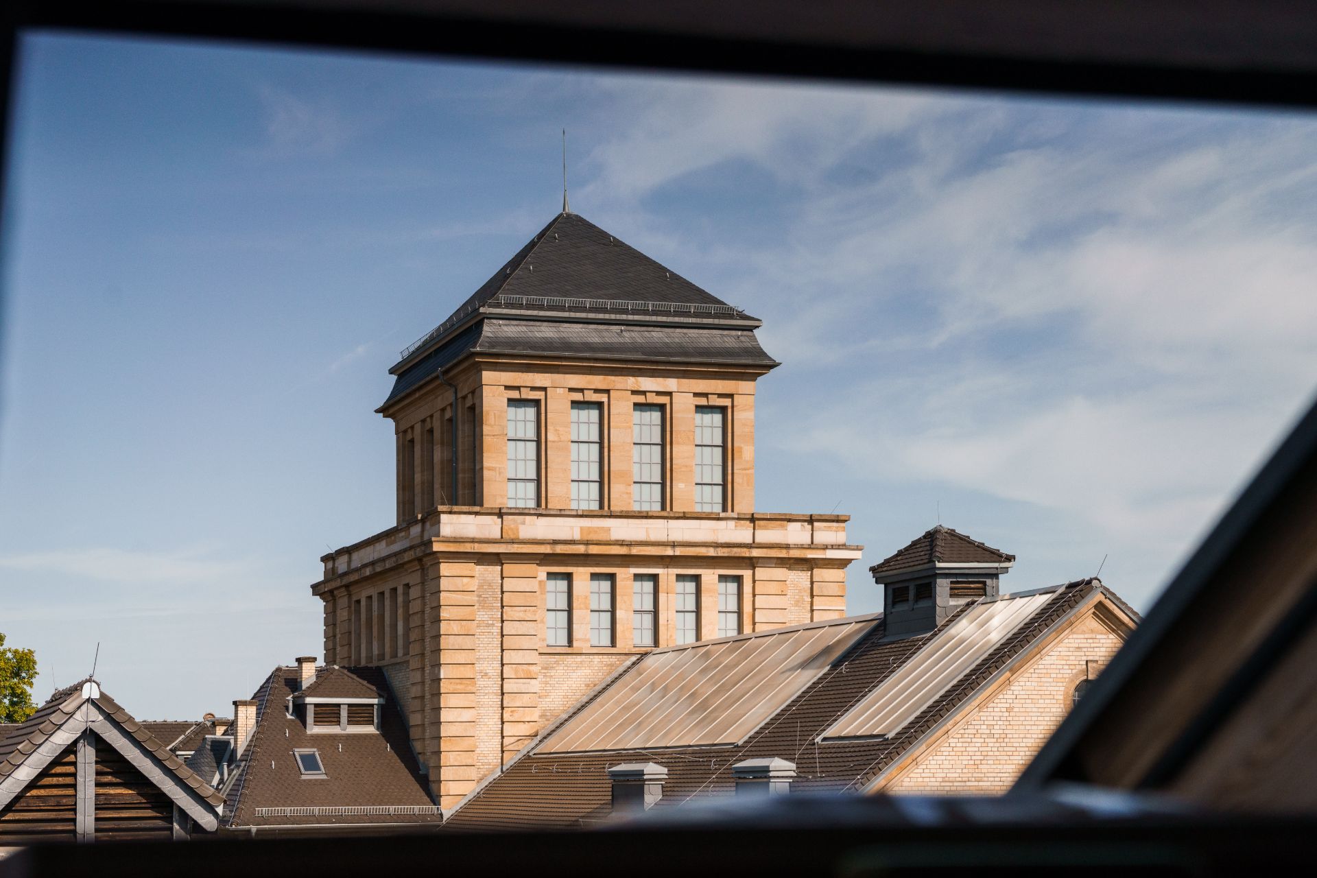 Blick aus dem Fenster auf ein großes, mehrstöckiges Gebäude mit Ziegeldach und Turm.