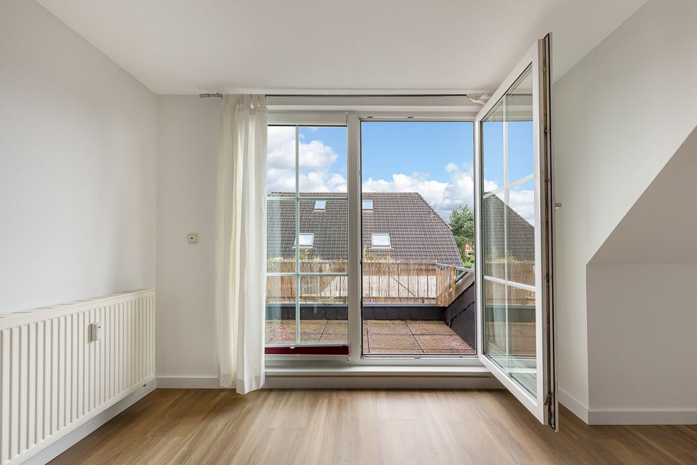 Helles Zimmer mit Holzboden, Heizkörper und großer Tür zur Terrasse mit Blick aufs Nachbarhaus.