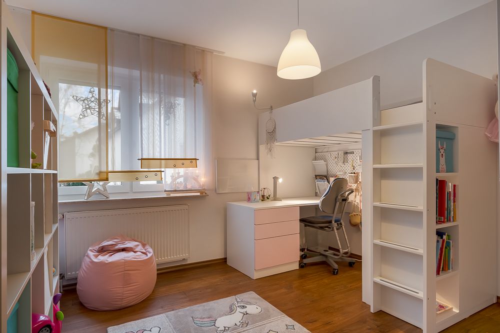 Helles Kinderzimmer mit Hochbett, Schreibtisch, Regal und Sitzsack vor dem Fenster.